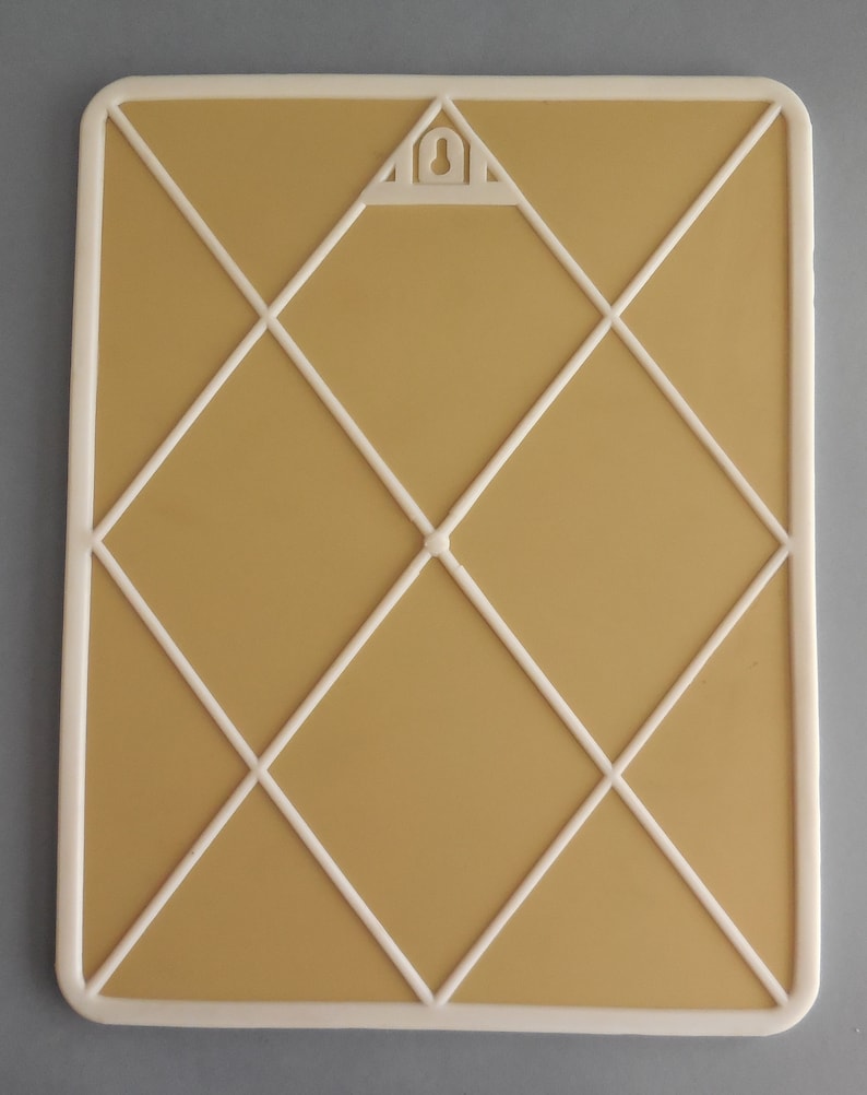 May include: Rectangular memo board with a cream-colored frame and a tan interior. White lines form a diamond pattern across the surface. A triangular hanger is at the top center. The board is designed for displaying notes, photos, or other items.