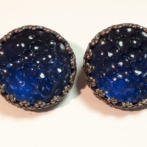 May include: A pair of blue glass earrings with a silver metal setting. The glass is textured and has a honeycomb pattern.
