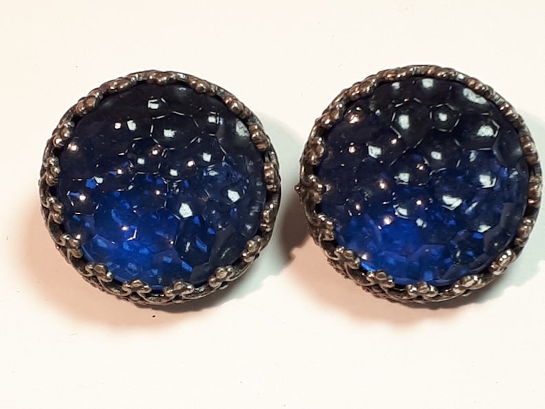 May include: A pair of blue glass earrings with a silver metal setting. The glass is textured and has a honeycomb pattern.