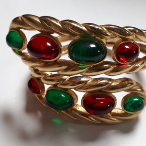 Puede incluir: Un brazalete de oro con un dise&ntilde;o de cuerda trenzada y piedras de vidrio rojo y verde.