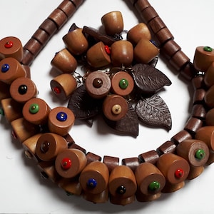Peut inclure: Un collier en bois avec des perles brunes et des accents colorés. Le collier est assorti à une broche assortie avec des feuilles en cuir brun et des glands en bois.