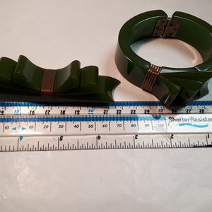 May include: A set of two green Bakelite jewelry pieces. A large green bangle bracelet with a gold metal clasp and a smaller green bow brooch with a gold metal accent.