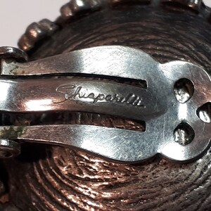 May include: Silver tone clip-on earrings with a textured design and the inscription "Shiparilla" on the back.