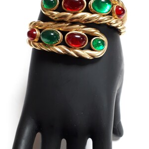 Puede incluir: Un brazalete de oro con un dise&ntilde;o de cuerda trenzada y piedras ovaladas rojas y verdes alternas.