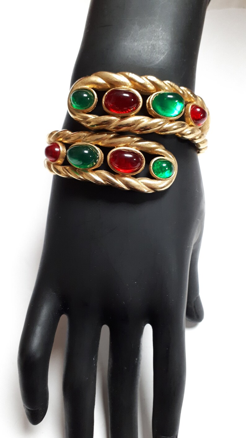 Puede incluir: Un brazalete de oro con un dise&ntilde;o de cuerda trenzada y piedras ovaladas rojas y verdes alternas.