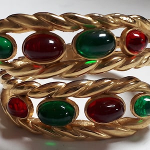 Puede incluir: Un brazalete de oro con un dise&ntilde;o de cuerda trenzada y piedras cabuj&oacute;n rojas y verdes alternas.