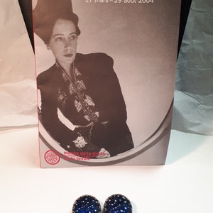 May include: A pair of blue glass earrings with a silver metal frame. The earrings are oval shaped and have a textured surface.