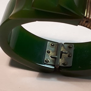 May include: A green plastic bangle bracelet with a metal clasp. The bracelet is made of two pieces that snap together.