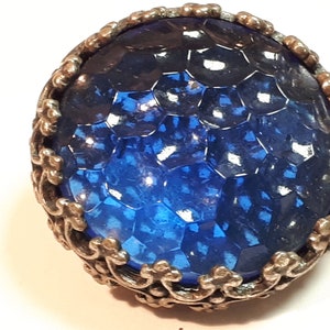 May include: A blue glass cabochon with a textured surface is set in a silver filigree frame.