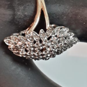 May include: A silver ring with a fan-shaped design set with small, sparkling stones.