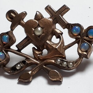 May include: A gold-toned brooch with a heart, anchor, and cross design. The brooch is decorated with opals and pearls.