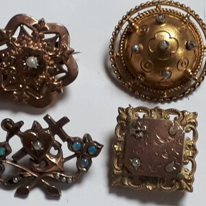 May include: Four antique gold brooches with pearl and opal accents. The brooches feature intricate designs, including a heart with crossed swords and anchors, a floral design, a round design with a raised center, and a square design with a raised center.