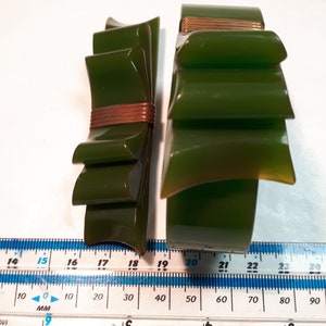 May include: Two green plastic bracelets with a gold accent. The bracelet on the left is a bow shape and the bracelet on the right is a layered design.