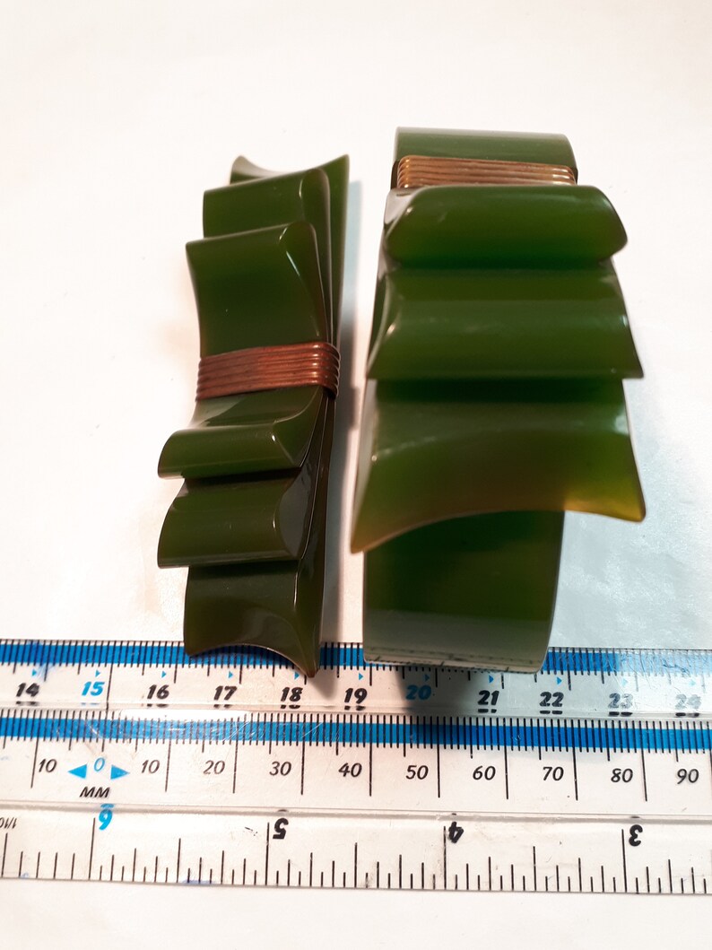 May include: Two green plastic bracelets with a gold accent. The bracelet on the left is a bow shape and the bracelet on the right is a layered design.