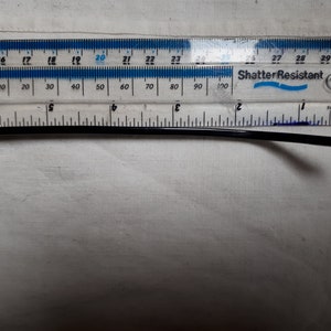 May include: Black sunglasses with a gold frame and dark lenses. The temple arm is measured with a ruler, showing a length of approximately 5 inches. The ruler is labeled "Shatter Resistant".