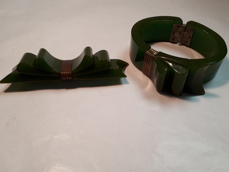 May include: A set of two green vintage bakelite jewelry pieces. A bow-shaped brooch with a brown center and a wide bangle bracelet with a gold-toned accent.