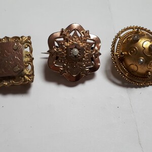 May include: Three antique gold brooches with pearl accents. The brooches are in the shape of a square, a flower, and a circle.
