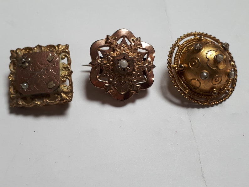 May include: Three antique gold brooches with pearl accents. The brooches are in the shape of a square, a flower, and a circle.