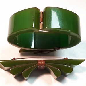 May include: A set of two vintage green Bakelite jewelry pieces. A wide green bangle bracelet with a gold-tone clasp and a matching green bow brooch with a brown metal center.