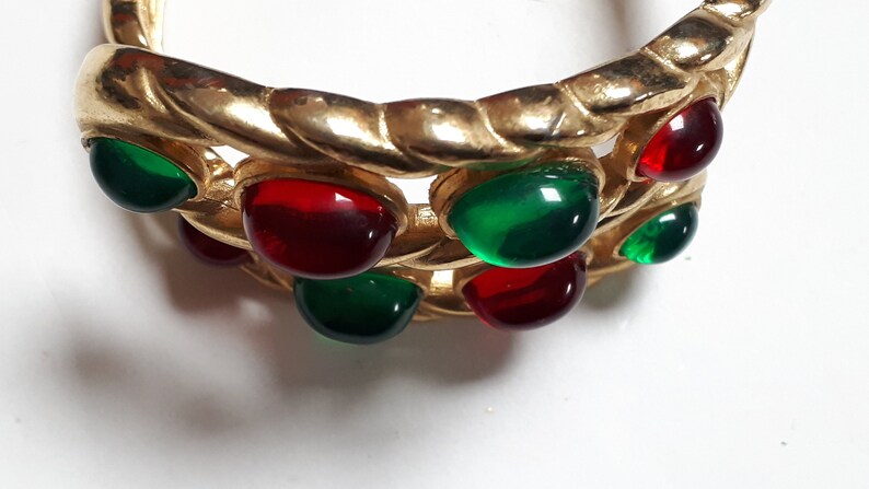 Puede incluir: Pulsera de tono dorado con piedras cabuj&oacute;n rojas y verdes.