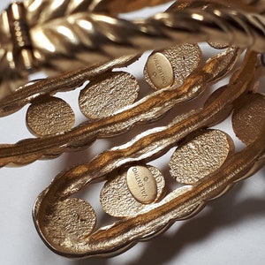 Puede incluir: Un brazalete de tono dorado con un dise&ntilde;o de cuerda trenzada y una serie de c&iacute;rculos redondos en relieve. El brazalete est&aacute; marcado con "VALENTINO JEWELRY" en el interior.