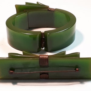 May include: A set of two vintage green bakelite jewelry pieces. A hinged bangle bracelet and a bow-shaped brooch.