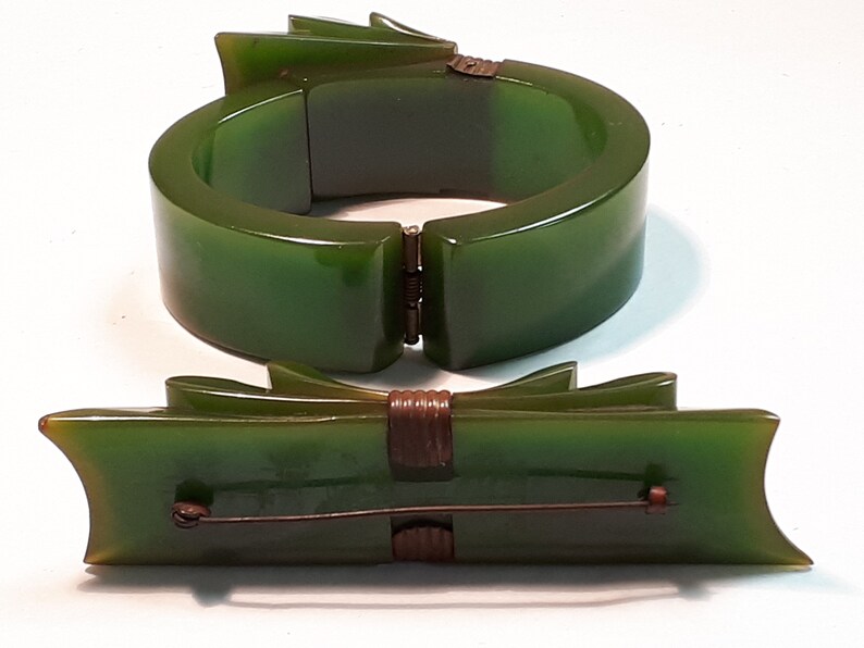 May include: A set of two vintage green bakelite jewelry pieces. A hinged bangle bracelet and a bow-shaped brooch.
