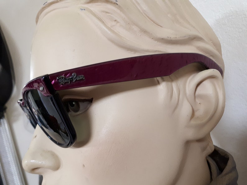 May include: Burgundy Ray-Ban sunglasses with black frames and dark lenses. The sunglasses are on a mannequin head.