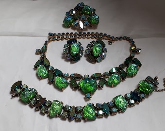 May include: A vintage jewelry set featuring a necklace, bracelet, earrings, and a brooch. The set showcases large, iridescent green stones set in a gold-tone metal. The stones have a textured, organic appearance, and the set is displayed on a white surface.