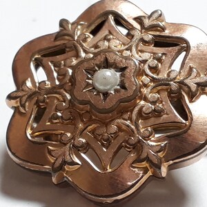 May include: A gold-toned brooch with a delicate floral design and a single pearl in the center.