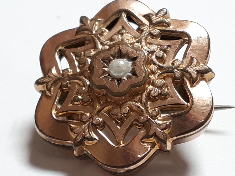 May include: A gold-toned brooch with a delicate floral design and a single pearl in the center.