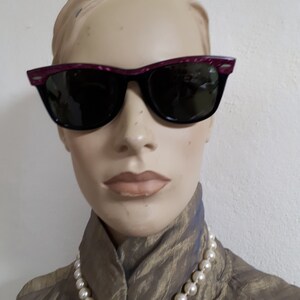 May include: A mannequin wearing a gold-colored blouse with a pearl necklace and black sunglasses with a pink frame.