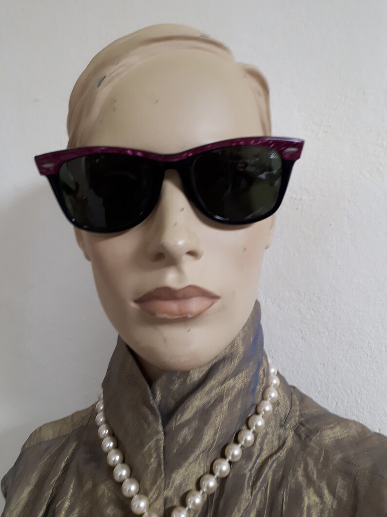 May include: A mannequin wearing a gold-colored blouse with a pearl necklace and black sunglasses with a pink frame.