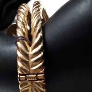 Puede incluir: Un brazalete dorado con un dise&ntilde;o de cuerda. El brazalete est&aacute; hecho de dos bandas entrelazadas.
