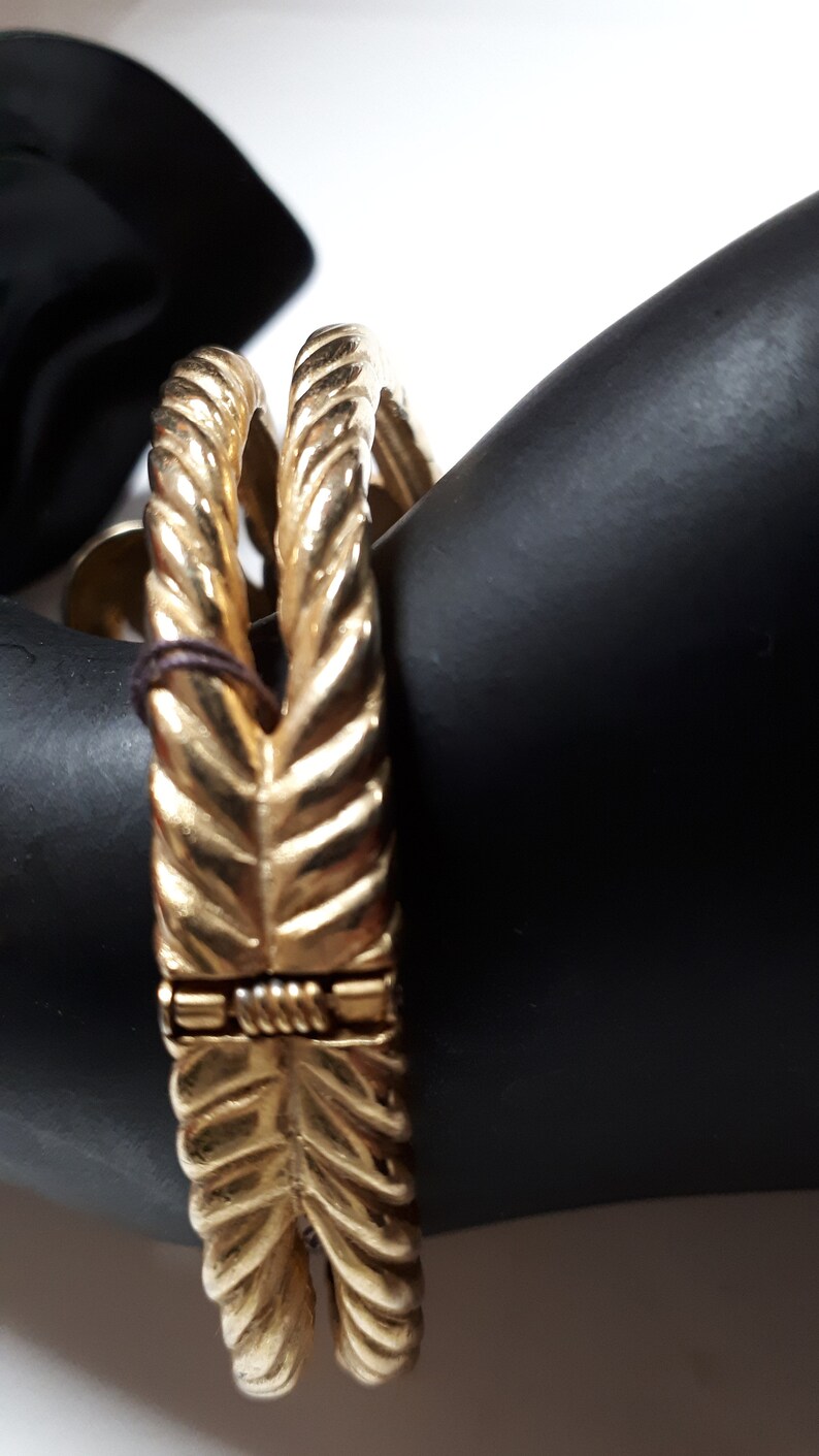 Puede incluir: Un brazalete dorado con un dise&ntilde;o de cuerda. El brazalete est&aacute; hecho de dos bandas entrelazadas.