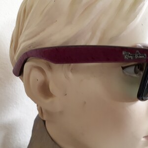 May include: A pair of dark purple Ray-Ban sunglasses with black lenses. The sunglasses are on a mannequin's head.