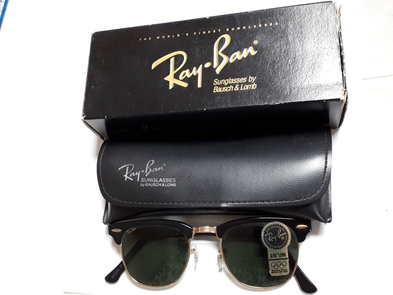May include: Black Ray-Ban sunglasses with gold-tone accents, green lenses, and a black leather case. The sunglasses are displayed with their original black box, which reads "THE WORLD'S FINEST SUNGLASSES".