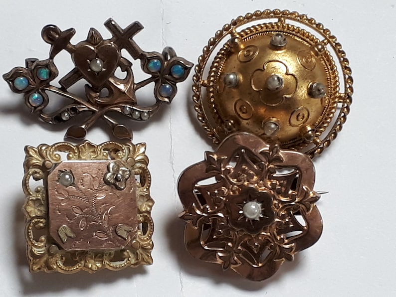 May include: Four antique gold brooches with pearl and opal accents. The brooches feature intricate designs including a heart, anchor, cross, and floral motifs.
