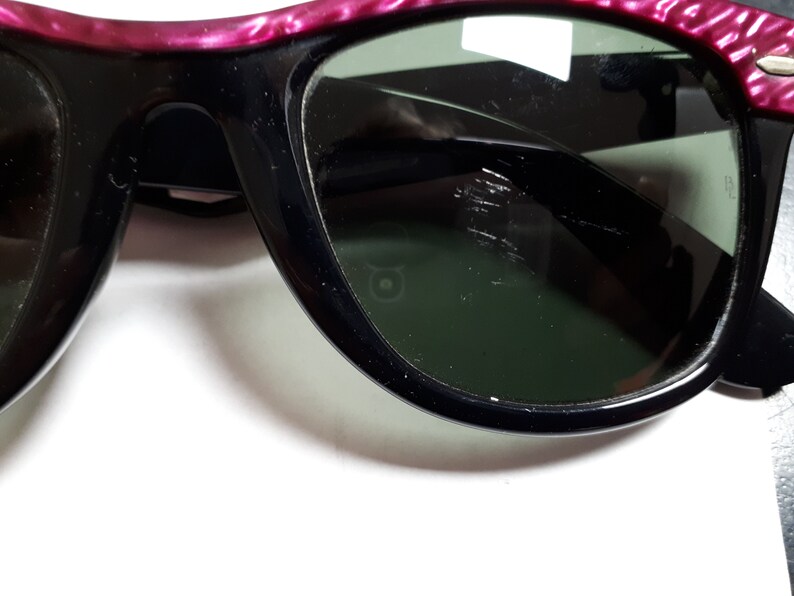 May include: A pair of black sunglasses with pink and silver frames. The lenses are dark green and have some scratches.
