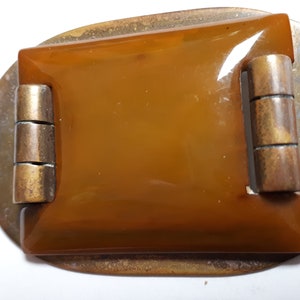 May include: A vintage amber glass buckle with a brass frame and a hinged closure. The buckle is oval shaped and has a smooth, polished finish.