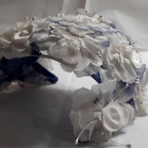 Könnte beinhalten: Ein weiß-blaues Blumenhaarband mit silbernen Drahtverzierungen. Das Haarband besteht aus Stoffblumen und ist perfekt für eine Hochzeit oder einen besonderen Anlass.