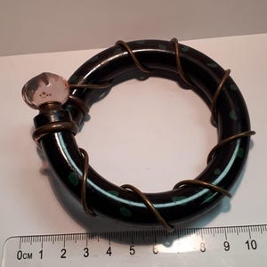 May include: A black and green ring with a copper wire wrapped around it. The ring has a clear glass bead on top.