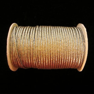 May include: A spool of gold and silver metallic cord. The cord is wound tightly around a cardboard spool.