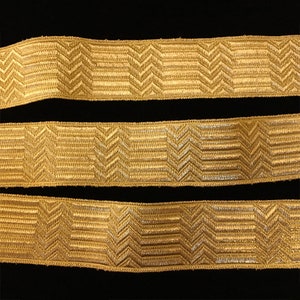 May include: Three pieces of gold trim with a chevron pattern. The trim is woven and has a subtle sheen.