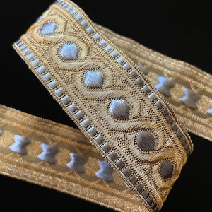 May include: Gold and silver trim with a geometric pattern. The trim is woven and has a raised texture.