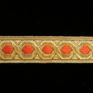 May include: Gold trim with a repeating pattern of red ovals. The trim is woven and has a slightly raised texture.