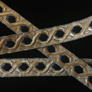 May include: Gold and black trim with a repeating pattern of oval shapes. The trim is woven with a metallic thread.