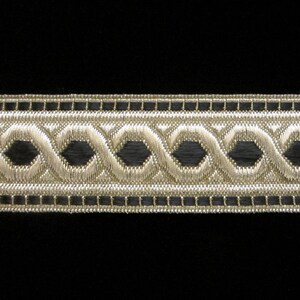 May include: A close-up of black and silver trim with a repeating pattern of interlocking circles. The trim is made of woven fabric and has a subtle sheen.