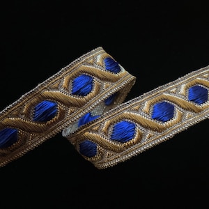May include: Gold and royal blue trim with a repeating geometric pattern. The trim features a raised design with a woven texture.