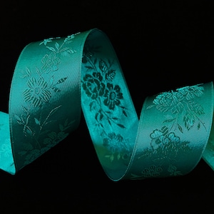 May include: Teal satin ribbon with a floral pattern. The ribbon is curled and twisted, showing off the intricate design.